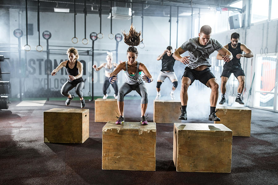 Athletic people jumping on crates during cross training in a health club Photograph by Skynesher
