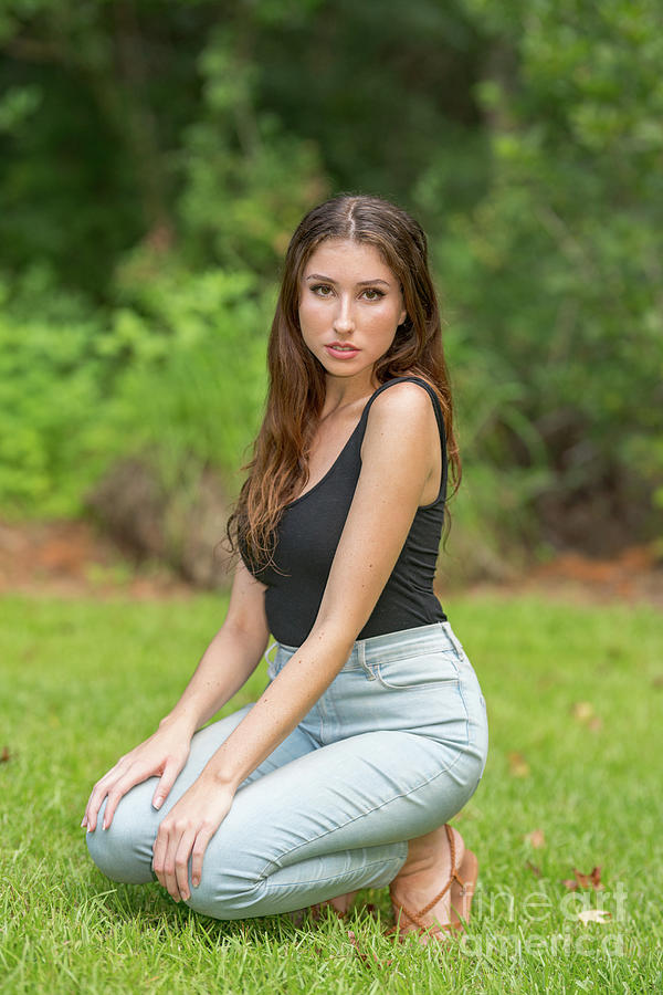 Attractive woman squatting in a park scene wearing tank top and ...