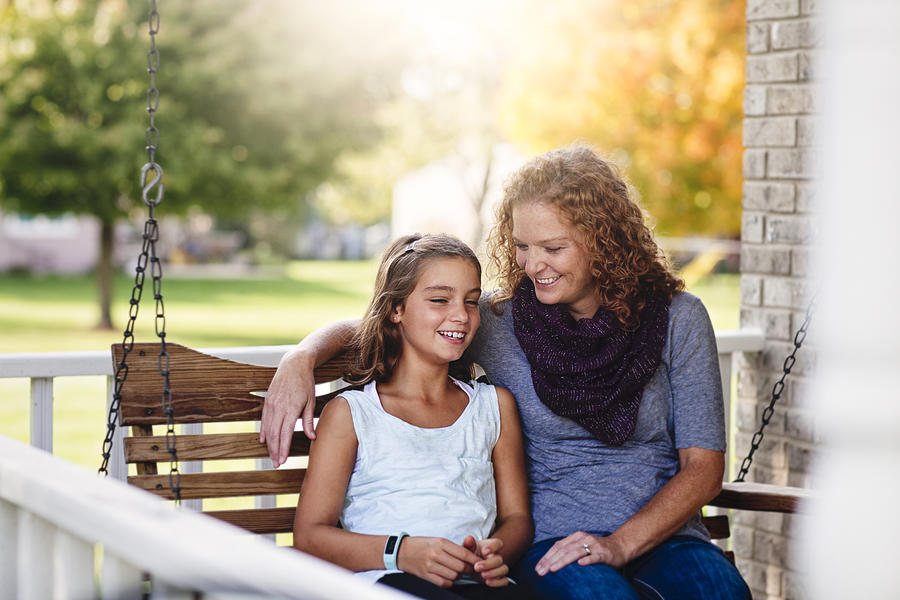 Aunt and niece sitting on porch swing, smiling Photograph by Rebecca Nelson