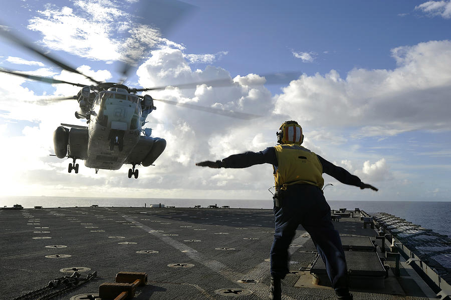 Aviation Boatswains Mate directs a CH-53E Super Stallion onto the flight deck of USS Harpers Ferry. Photograph by Stocktrek Images