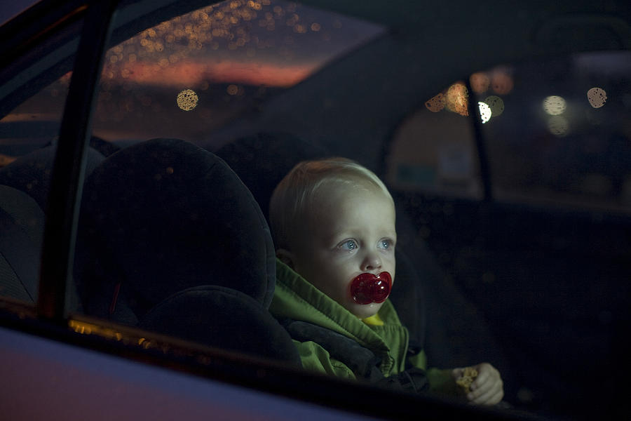 Baby boy (12-18 months) sitting in back seat of car, night Photograph by Johannes Kroemer