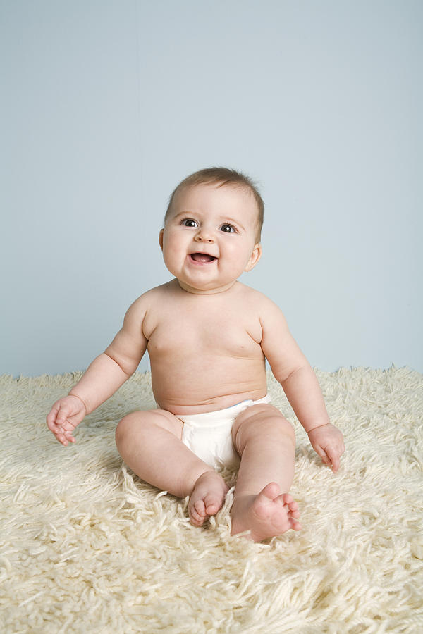 Baby boy (4-7 months) sitting on rug, smiling Photograph by Karen Moskowitz