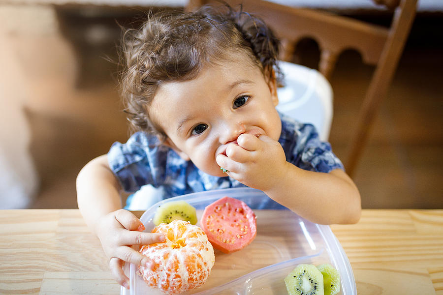 Baby boy eating tasty fruit Photograph by Capuski