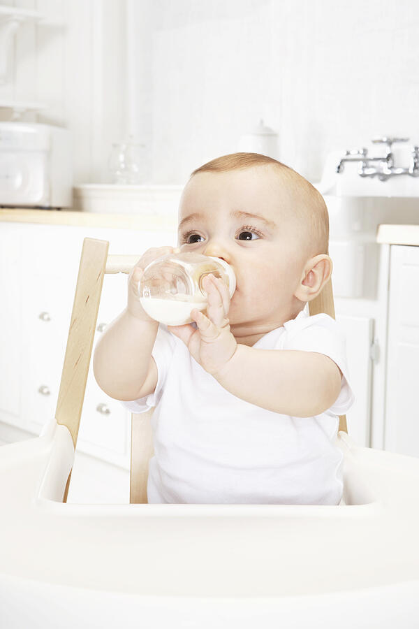 Baby girl (6-9 months) drinking bottle in high chair, close-up Photograph by James Woodson
