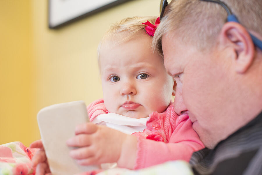 Baby girl holding smartphone with dad closed toher Photograph by Sollina Images