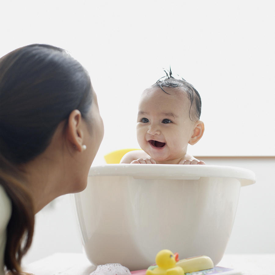 Baby girl in bathtub laughing at mother Photograph by Floresco Productions