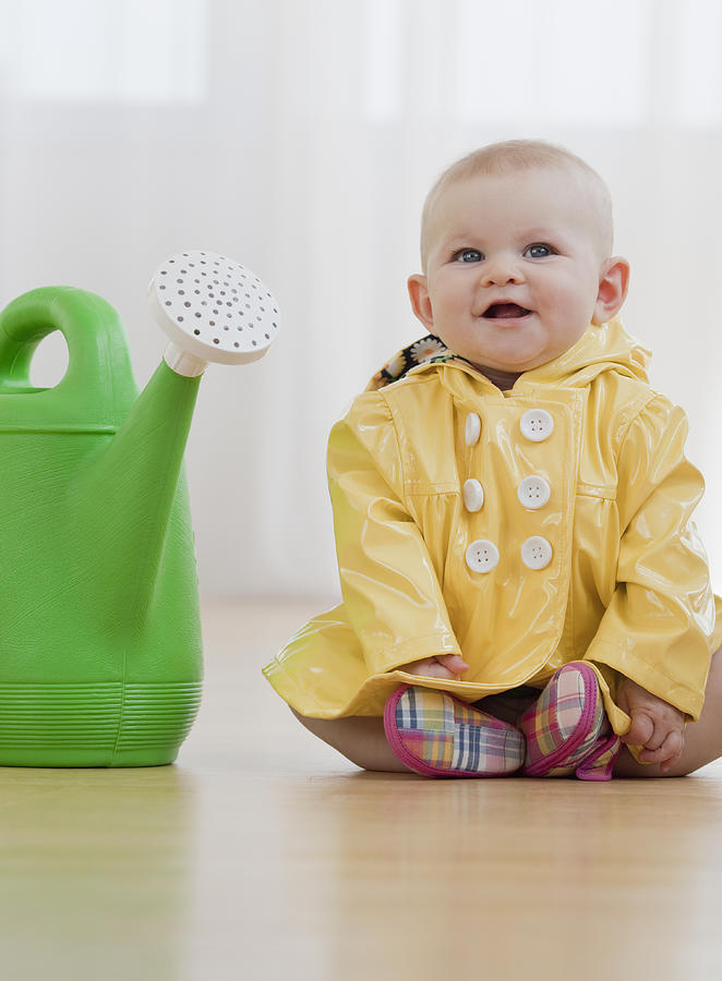 Baby girl in raincoat next to watering can Photograph by Jamie Grill