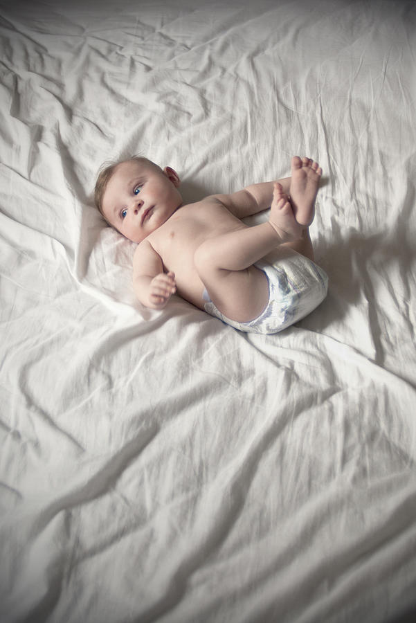 Baby in diaper lying on back with legs up Photograph by PhotoAlto/Neville Mountford-Hoare