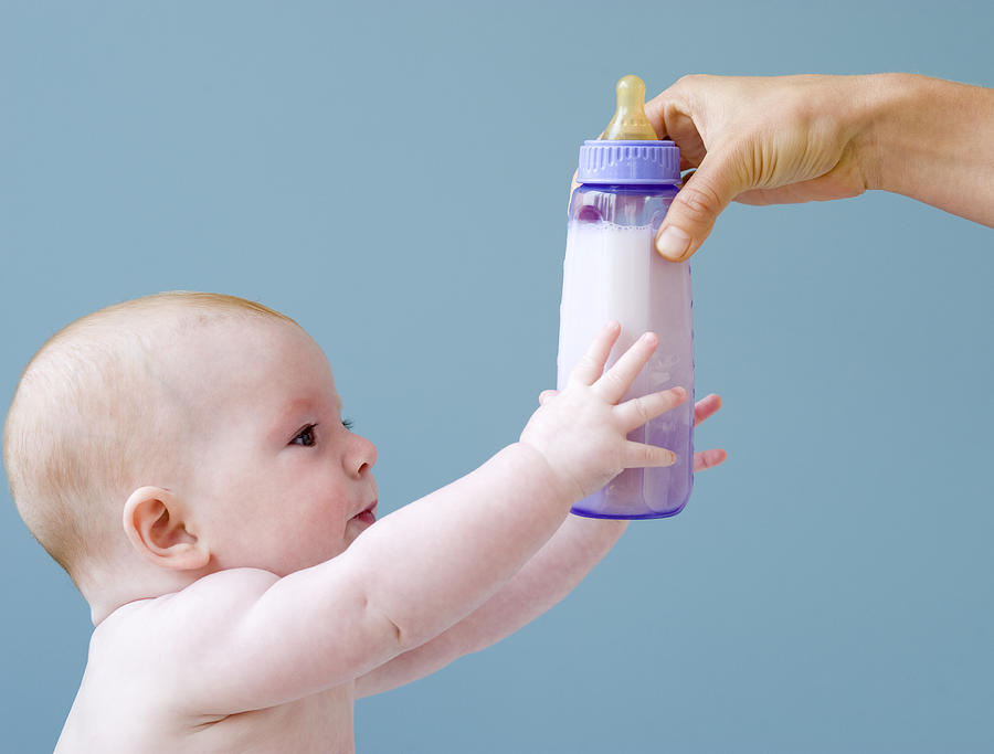 Baby reaching for bottle of milk from mother Photograph by Jamie Grill