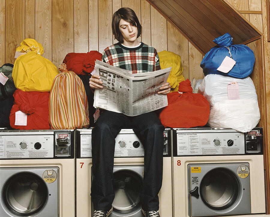 Bachelor Sitting On Top of a Washing Machine and Reading a Newspaper in a Launderette Photograph by Digital Vision.
