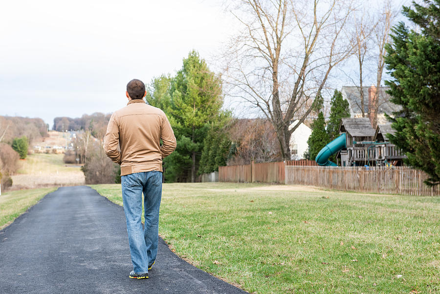 Back of young man walking on Sugarland Run Stream Valley Trail hike in Herndon, Northern Virginia, Fairfax county residential neighborhood in winter, spring, paved path road, houses Photograph by Krblokhin