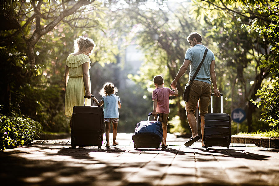 Back view of a family pulling their suitcases in nature. Photograph by Skynesher