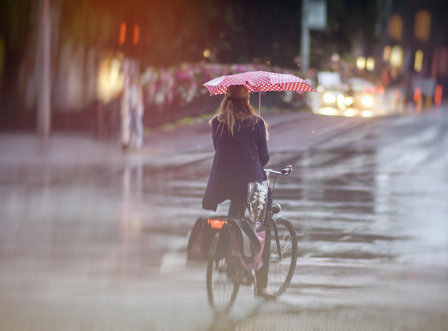 Back view of a woman bicycling in the rain with a red umbrella in Amsterdam city. Photograph by Daniel Hernanz Ramos