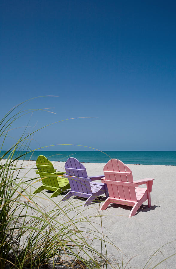 Back view of three pastel colored beach chairs on sand Photograph by LattaPictures