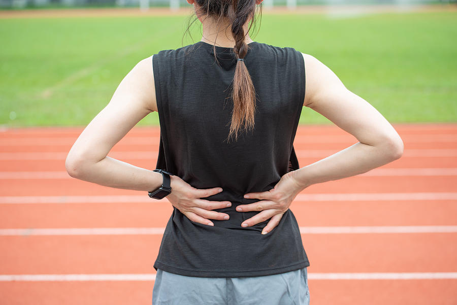 Back view of young runner woman suffering from Backache or Sore waist after running in the running track in stadium. Photograph by Boy_Anupong