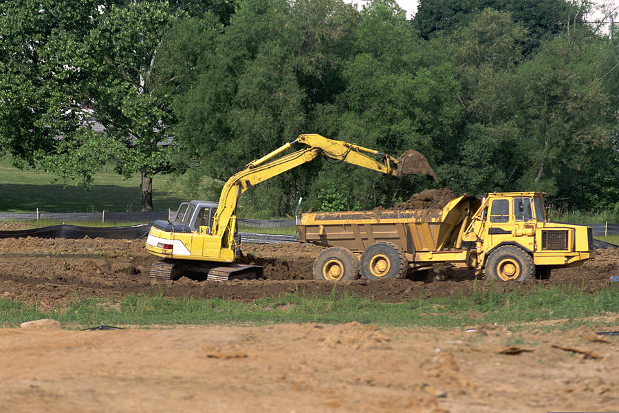 Backhoe unloading dirt from dump truck Photograph by Comstock Images