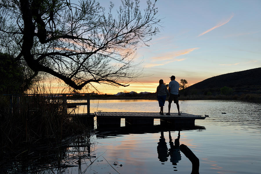 Backlit couple watching the sunset on a dock, Patagonia Lake State Park, Arizona, USA Photograph by Kevin Oke
