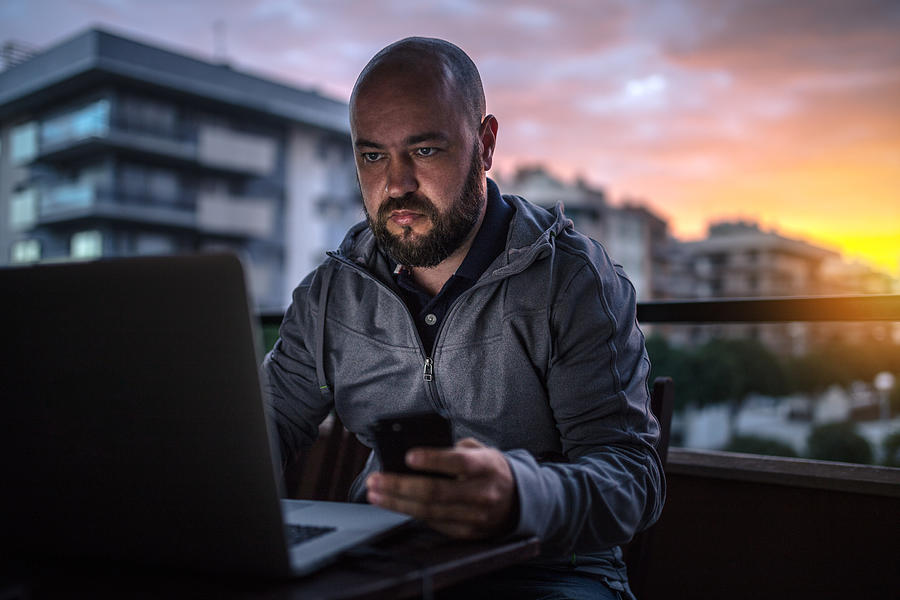 Bald and bearded men uses laptop and smartphone at sunset Photograph by Sankai