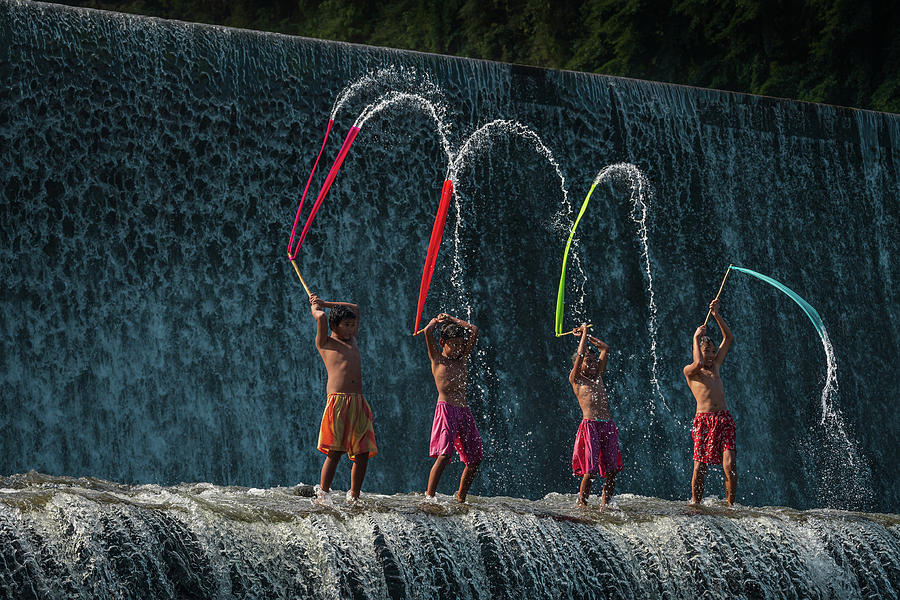 Balinese boys playing with colorful slayers in the Tukad Unda waterdam Photograph by Anges Van der Logt
