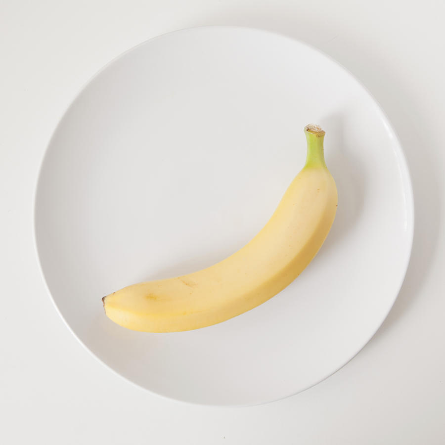 Banana on plate, studio shot Photograph by Jessica Peterson