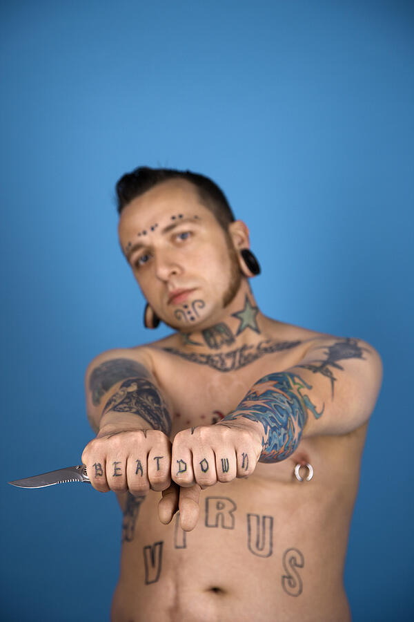 Barechested Caucasian mid-adult man with tattoos and piercings holding knife. Photograph by Fotosearch