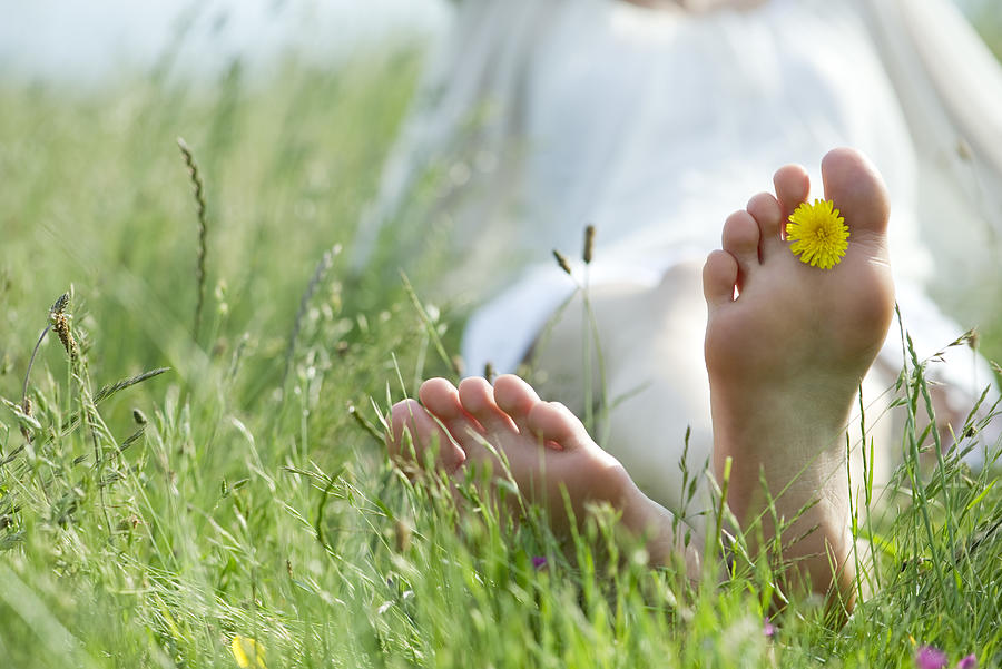 Barefoot woman sitting in grass, holding dandelion flower between toes Photograph by ZenShui/Laurence Mouton