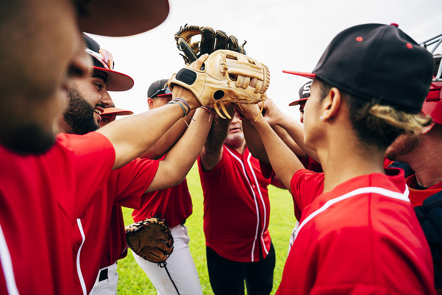 Baseball team coach and players raising gloves for high-five Photograph by JohnnyGreig