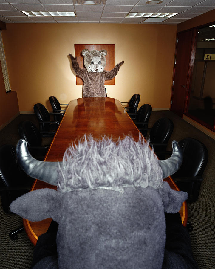 Bear and bull looking at each other across conference room table Photograph by Ryan McVay