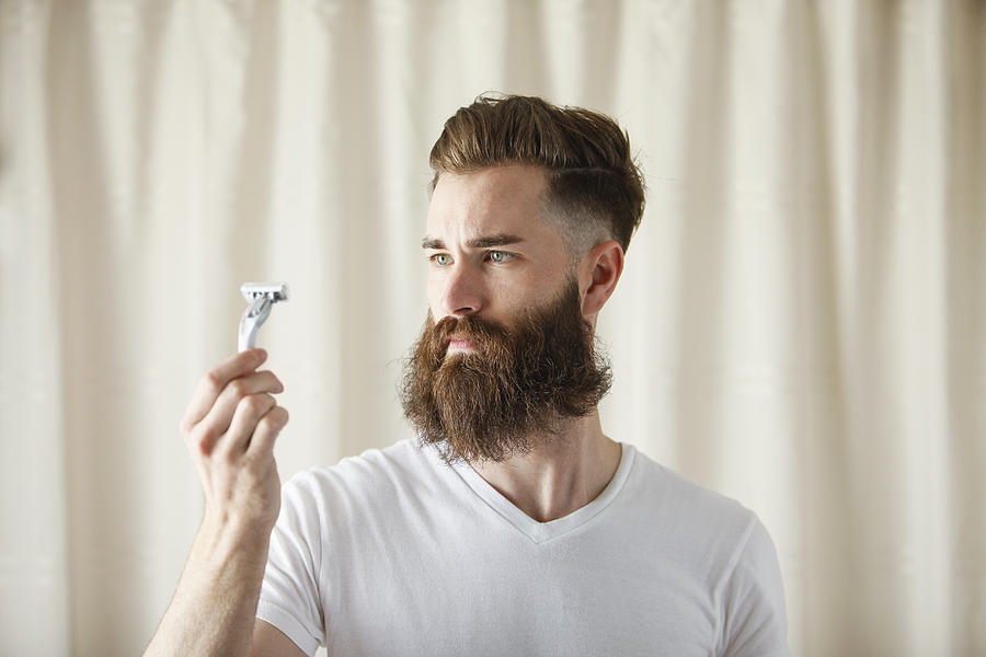Bearded Caucasian man examining razor Photograph by Mike Kemp