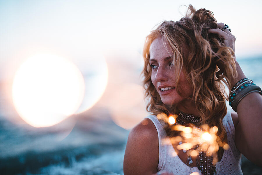 Beautiful boho girl celebrating with sparklers at beach at sunset Photograph by Wundervisuals