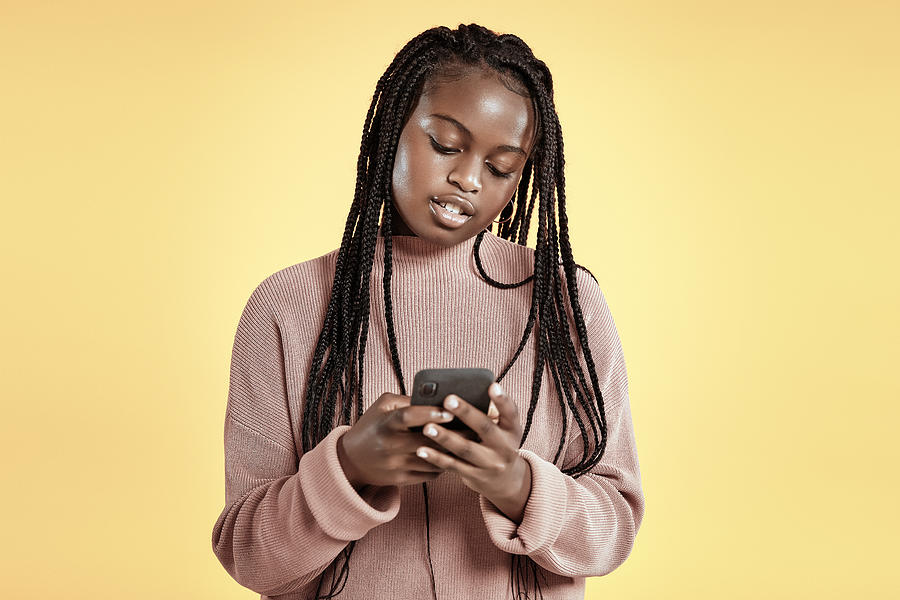 Beautiful teenager using smartphone on yellow background Photograph by Anna Frank