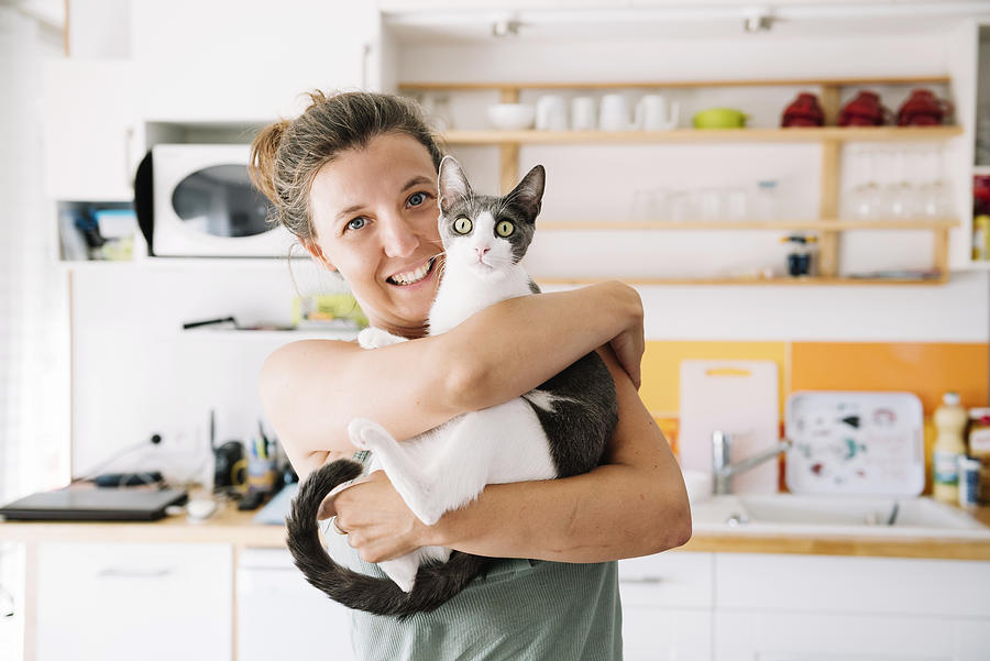 Beautiful woman holding a cute cat at home Photograph by Volanthevist