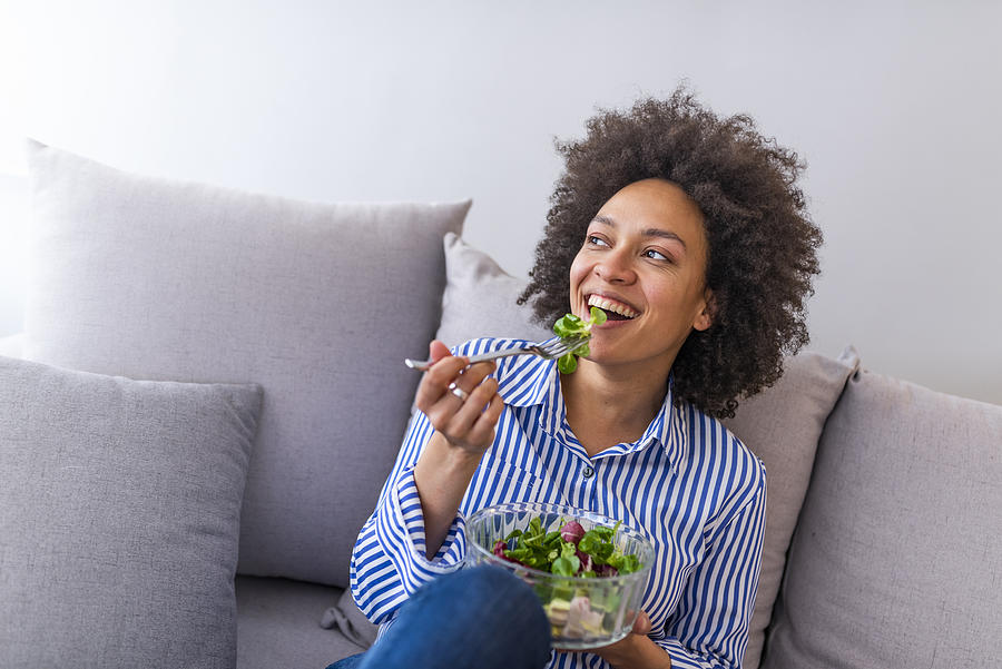 Beautiful woman on the sofa eating a healthy salad Photograph by Dragana991