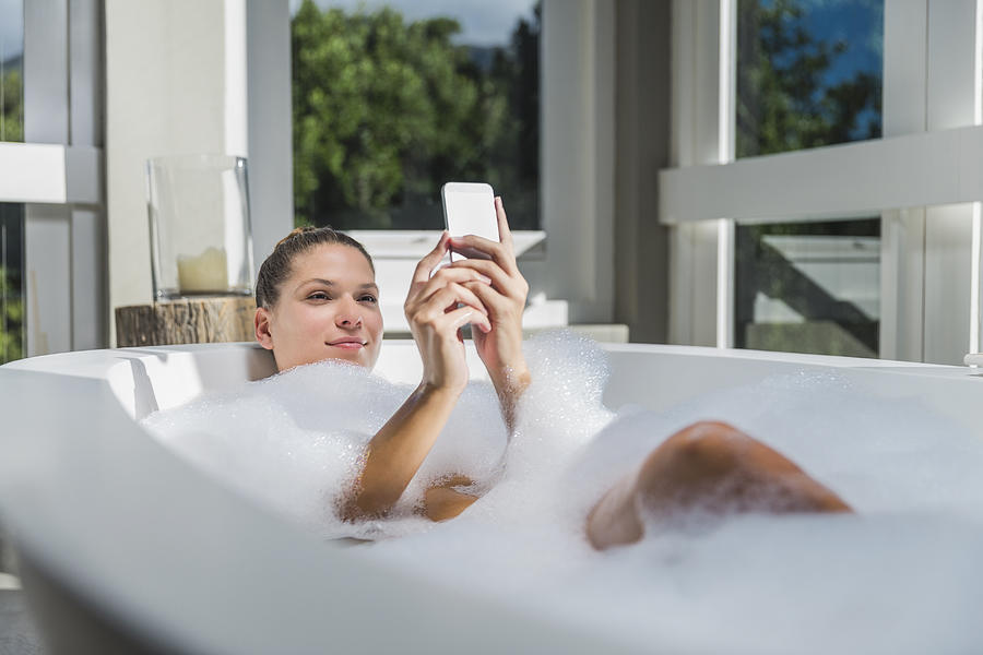 Beautiful woman using smart phone in bathtub Photograph by Portra