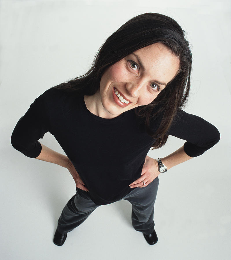 Beautiful Young Bruenette Caucasian Adult Female Wearing Dark Slacks And A Dark Shirt Has Her Hands On Her Hips As She Cocks Her Head And Looks Up At The Camera Smiling Photograph by Photodisc