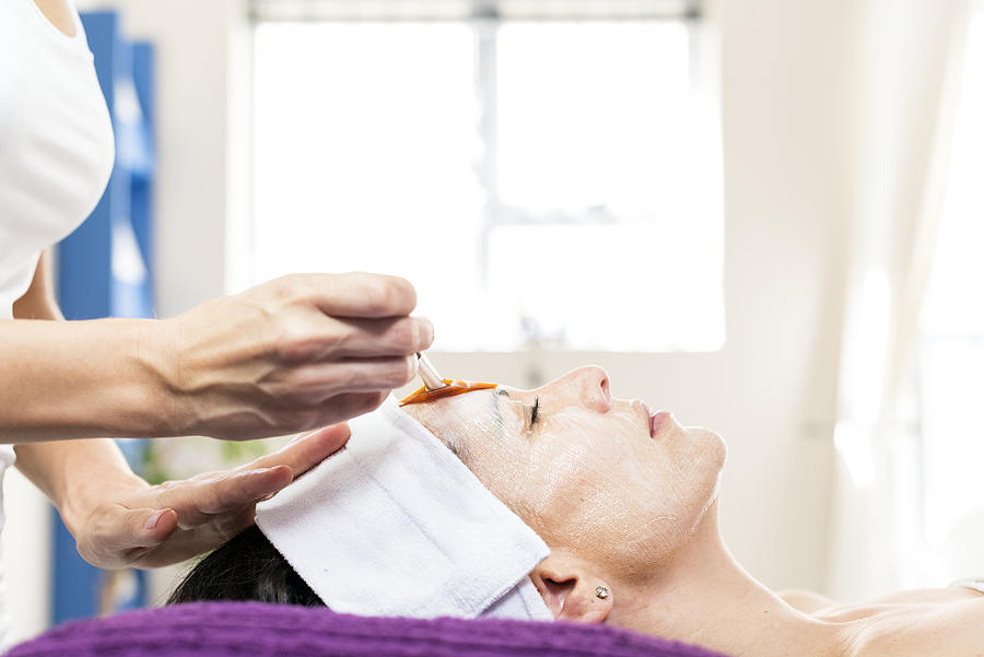 Beauty therapist applying a face mask to a client Photograph by PixelCatchers