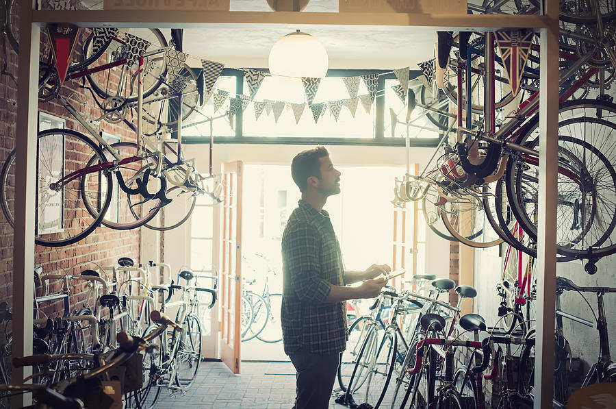 Bike Shop owner checks inventory with tablet Photograph by Superb Images