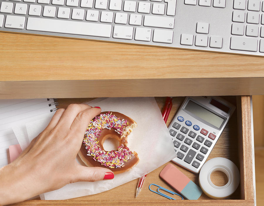 Binge eater hiding doughnut in desk drawer Photograph by Peter Dazeley