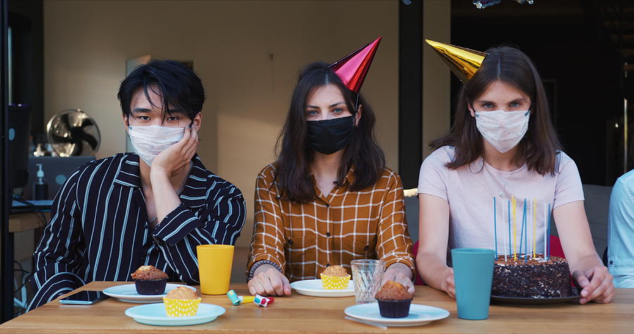Birthday party spoiled by COVID-19. Slide along sad upset multiethnic friends in masks at celebration table slow motion. Photograph by Vadim_Key