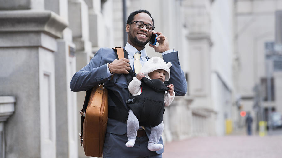 Black businessman with son in baby carrier talking on cell phone Photograph by Ariel Skelley