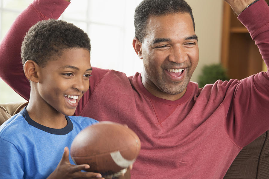 Black father and son watching sports in living room Photograph by Ariel Skelley