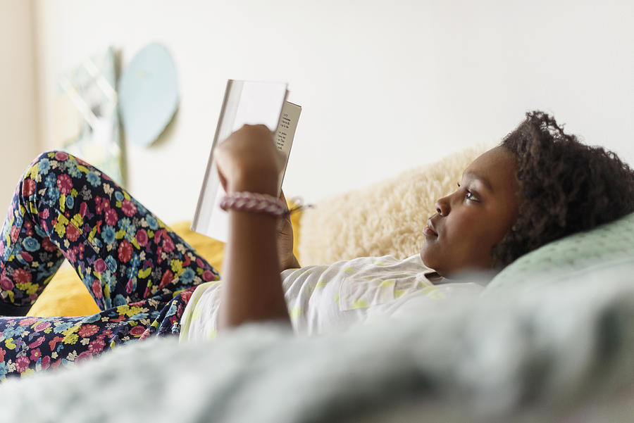 Black girl reading book on bed Photograph by JGI/Tom Grill