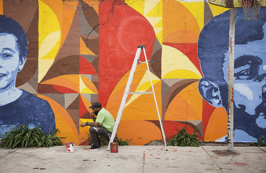 Black man sitting on ladder by mural Photograph by Hill Street Studios