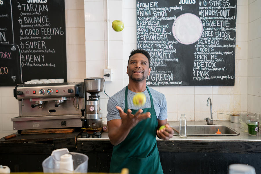 Black salesman working at a cafe juggling with fruits behind the counter having fun Photograph by Andresr