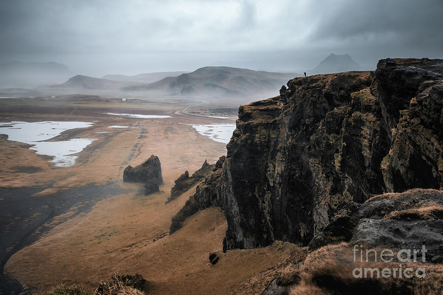Black sand beach, cliffs and mountains of Dyrholaey, Southern Iceland, in autumn. A photographer is silhouetted on the cliff top. Photograph by Jane Rix