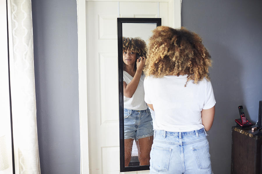 Black woman examining hair in mirror Photograph by Granger Wootz