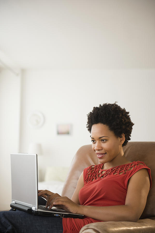 Black woman using laptop in armchair Photograph by JGI/Jamie Grill