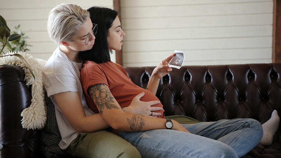 Blonde runs hands on pregnant girlfriend belly at home Photograph by Teraphim