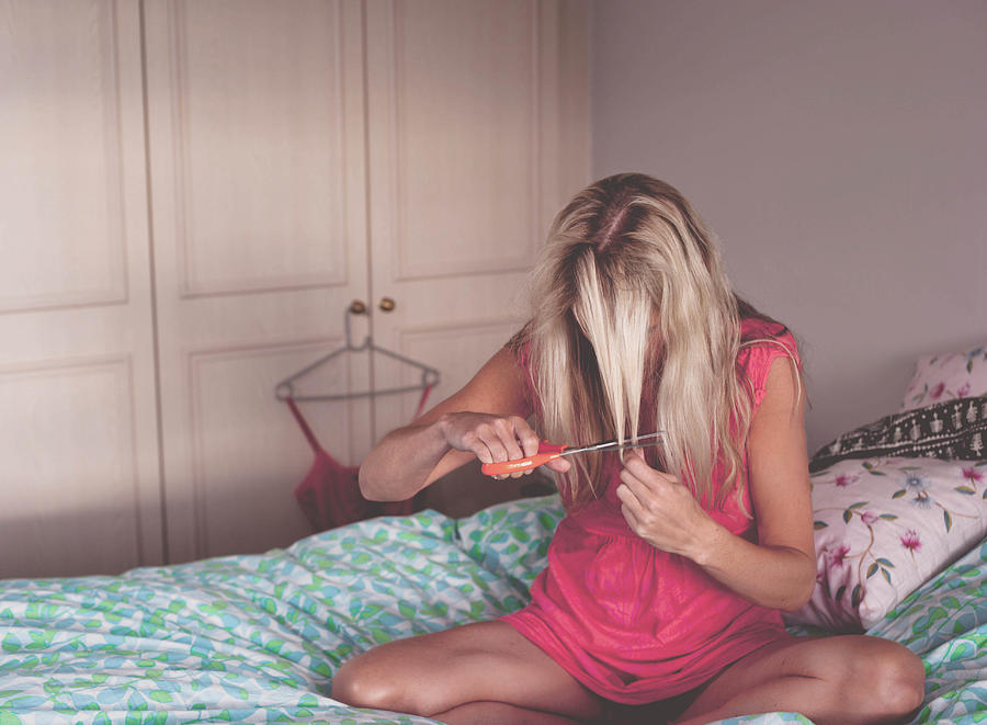 Blonde woman sitting on bed cutting her hair Photograph by Photography by Charlotte Trotman