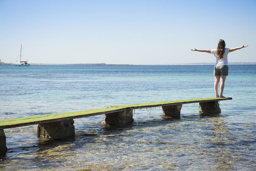 Blonde woman standing on dock with open arms looking at the Mediterranean Sea, Ibiza Photograph by Carlos Ciudad Photos
